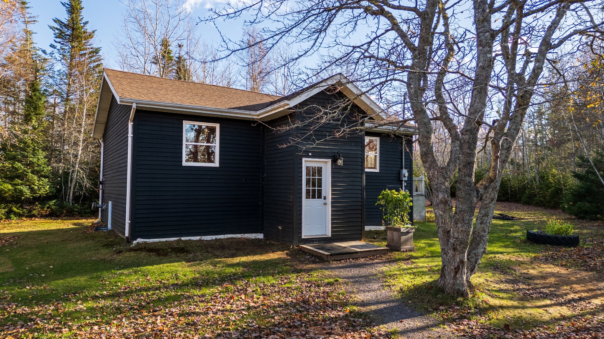 Black-sided country home with a small covered porch, set on a green rural lot framed by trees.